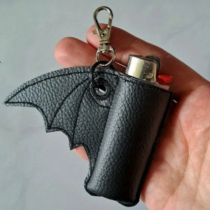 Black leather bat-shaped lighter case with a keychain clip held in a hand against a gray background.
