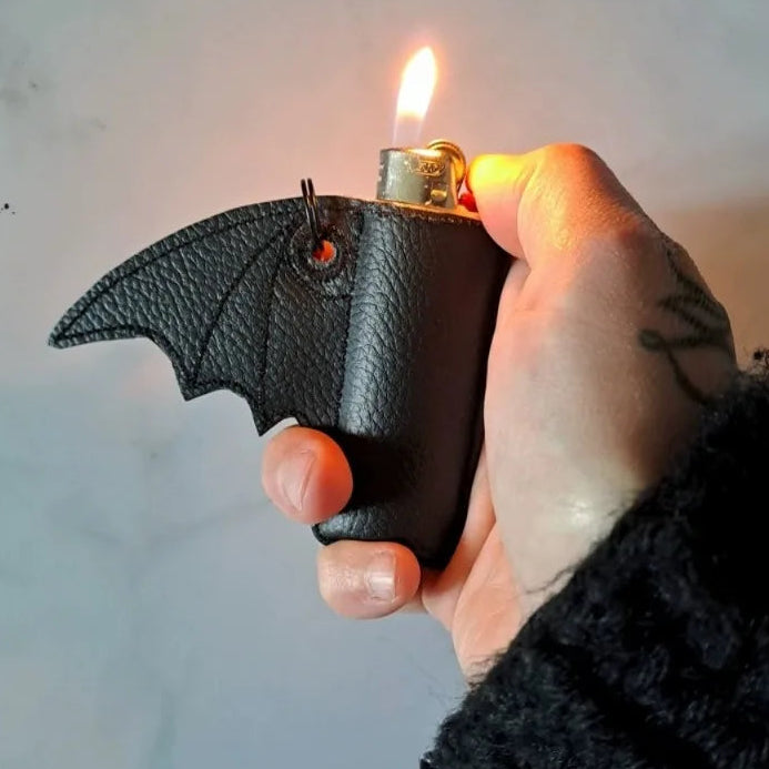 Hand holding a bat-shaped lighter with a lit flame against a neutral background